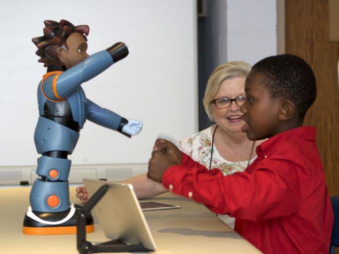 A child playing with a small robot and his teacher in classroom 